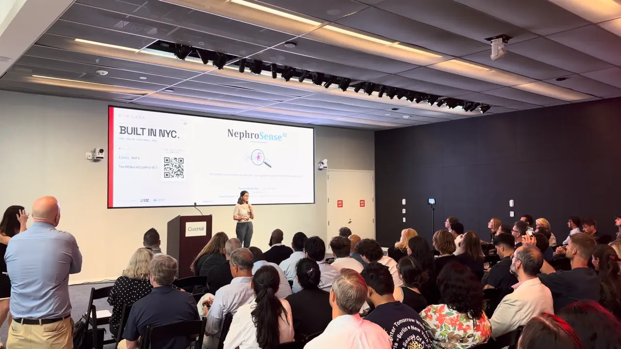 Poornima Dubey pitching on stage at Civic Hall in front of the NephroSense AI title slide, with a seated audience in the foreground